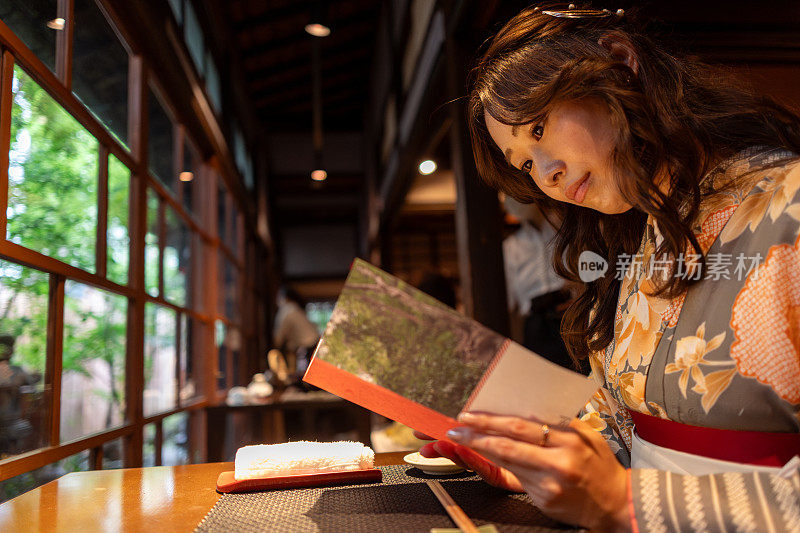 独自旅行的女人穿着和服/ Hakama在传统的日本咖啡馆阅读旅游指南